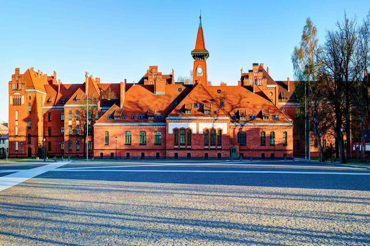 Historic red brick building with clock tower and spire in European town square, showcasing traditional German architecture
